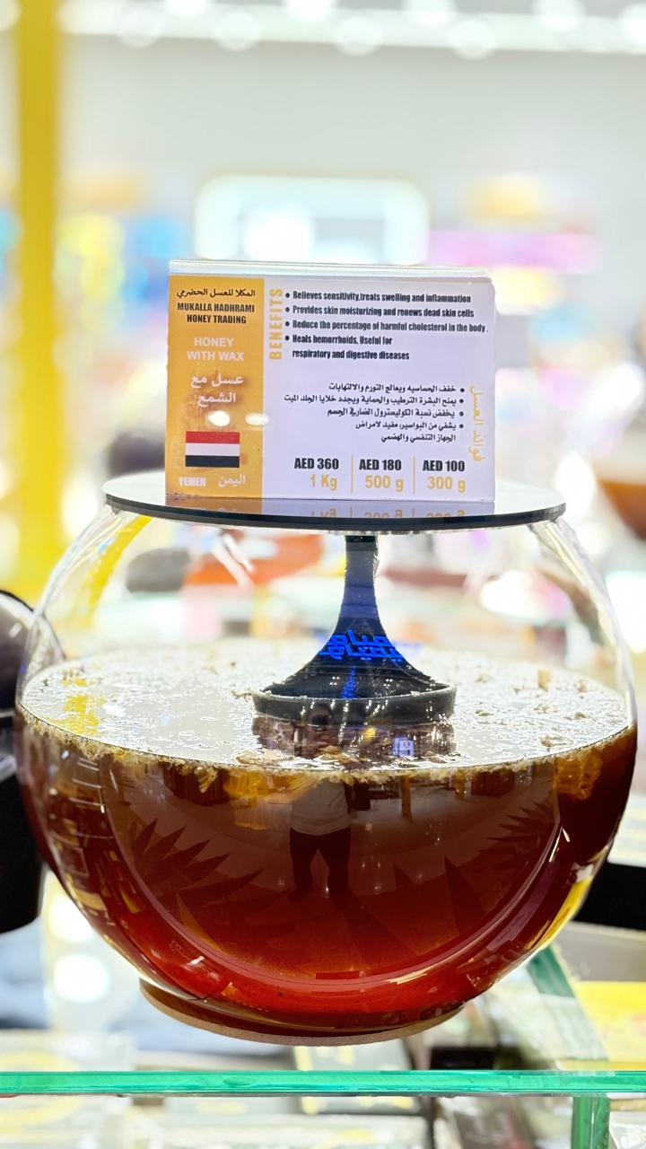 Honey with natural wax comb in a spherical glass jar with branded label.